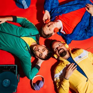 Zanadu Coverband München – die Bandmitglieder liegen in bunten Klamotten auf dem Boden
